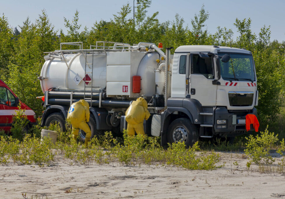 Mans with briefcase in protective hazmat suit, tank in the nature, which is all around